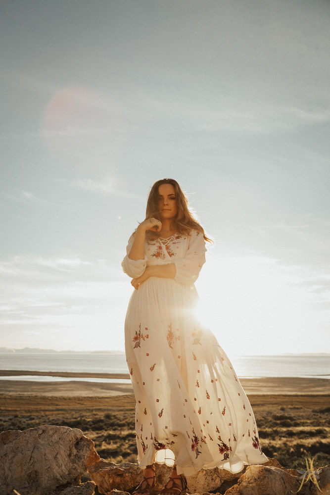 Woman standing in a white dress with the sun setting behind her