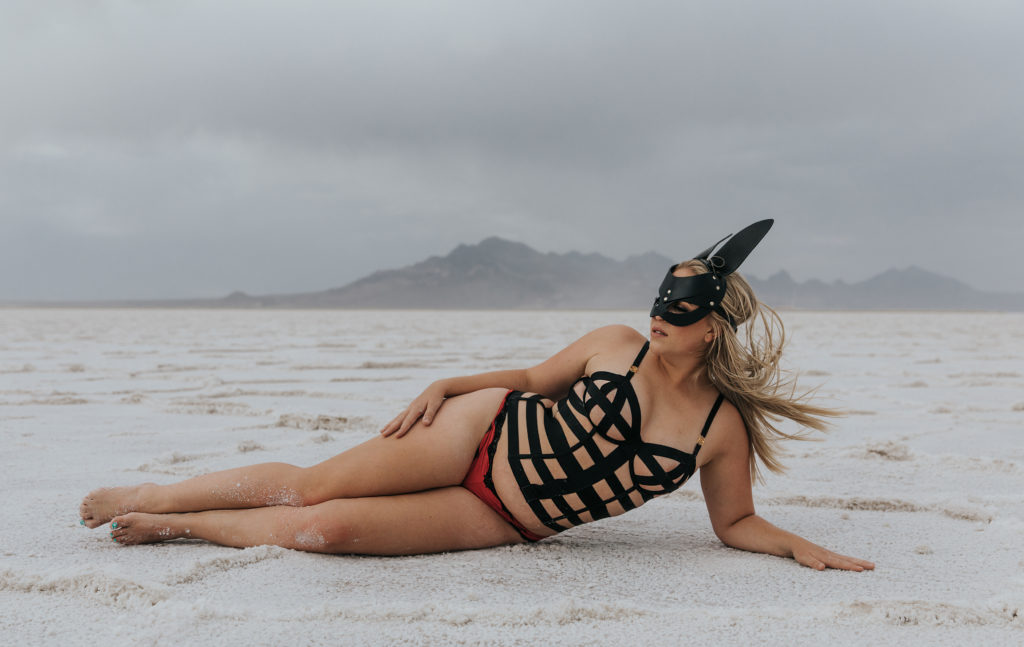 woman laying on the salt flats in a leather bunny mask and lingerie