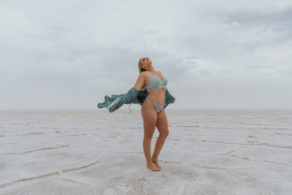 Outdoor boudoir shoot with woman standing in the wind during a storm at the Bonneville salt flats