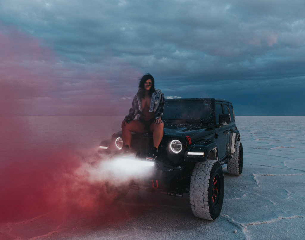 woman sitting on top of her car with a pink smoke bomb going off.