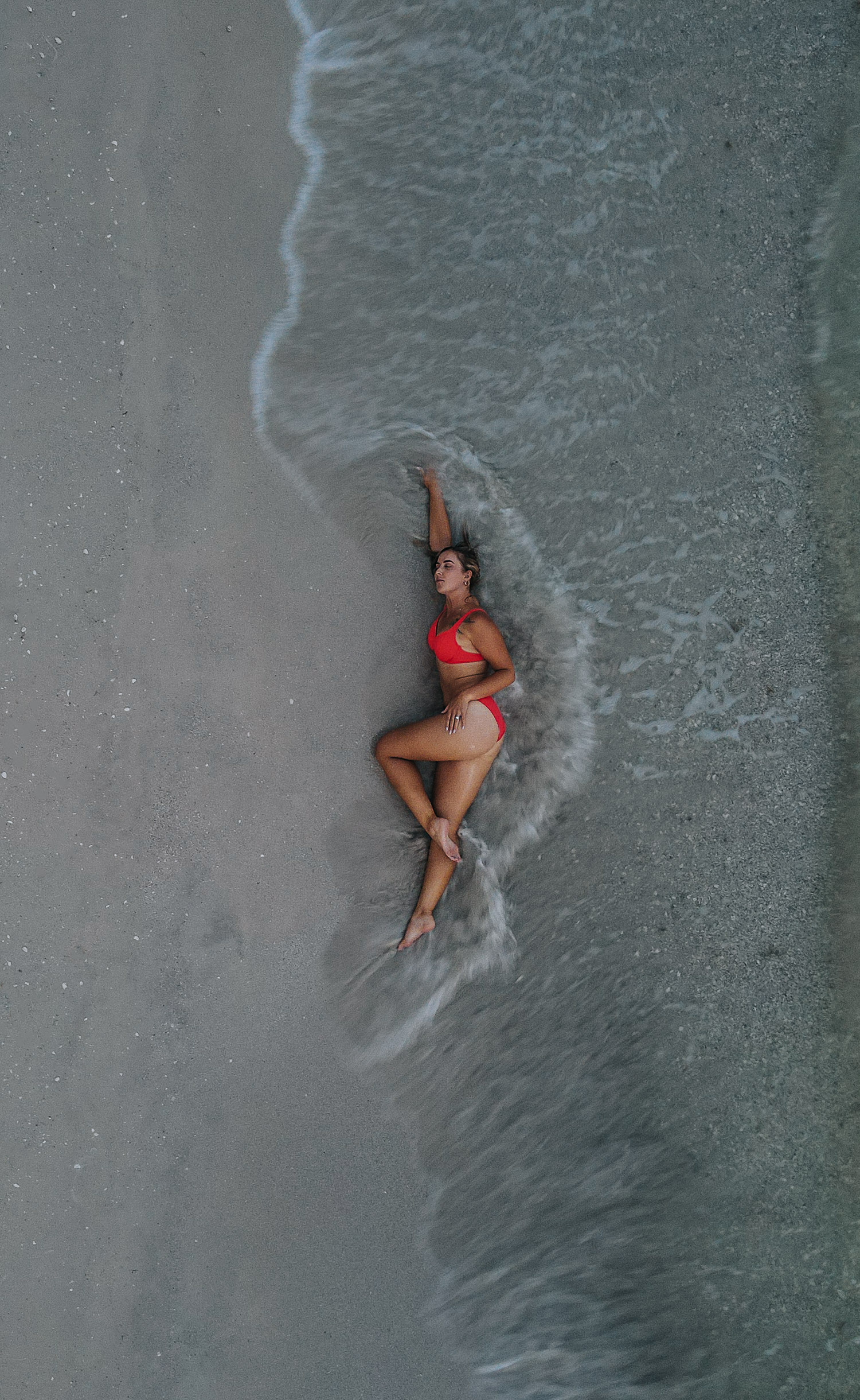 Woman laying in the waves and sand to get a drone shot photo