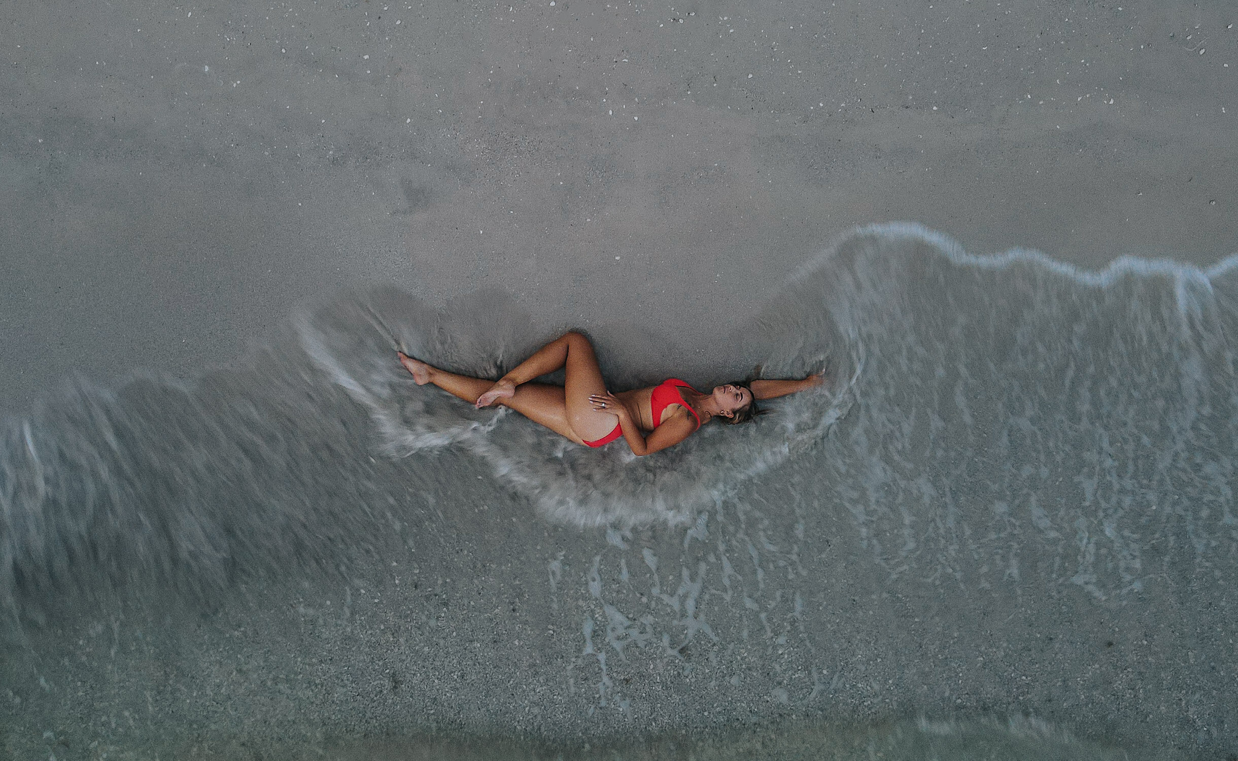 Woman laying in the waves and sand to get a drone shot photo