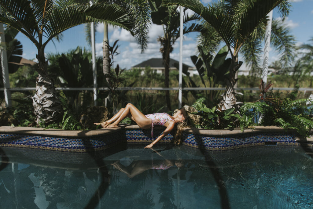 Woman laying on the side of the pool with one hand in the water and on in her hair.
